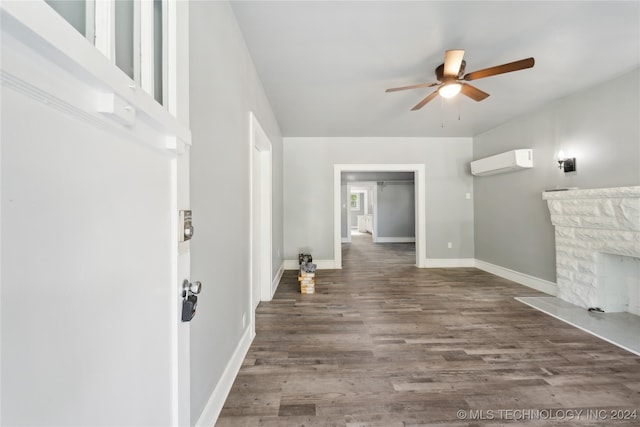 unfurnished living room featuring a stone fireplace, dark wood-type flooring, ceiling fan, and a wall mounted air conditioner