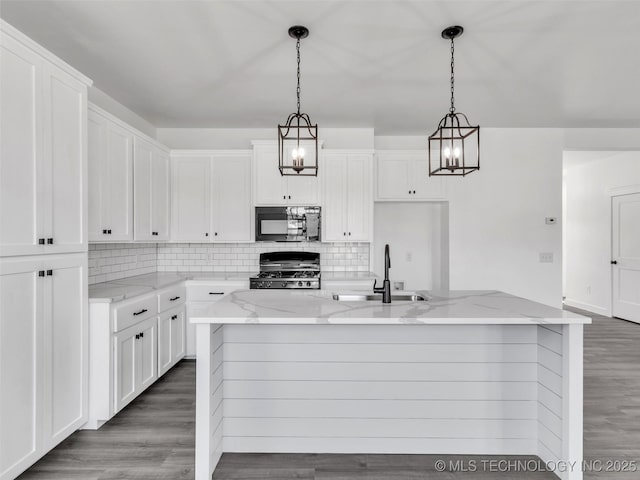 kitchen with white cabinetry, sink, stove, pendant lighting, and a center island with sink