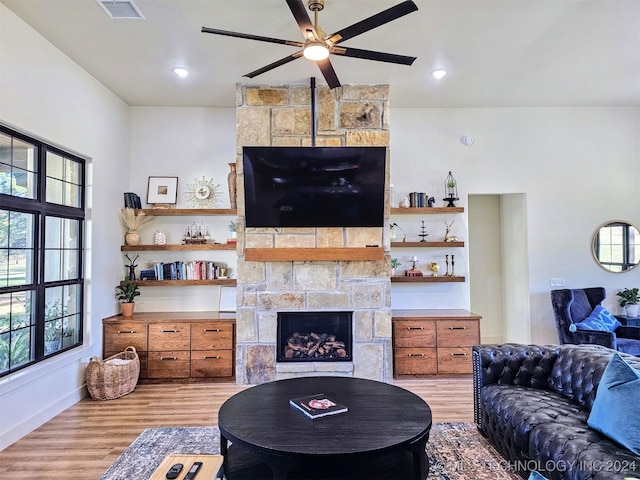 living room with ceiling fan, a stone fireplace, and light wood-type flooring