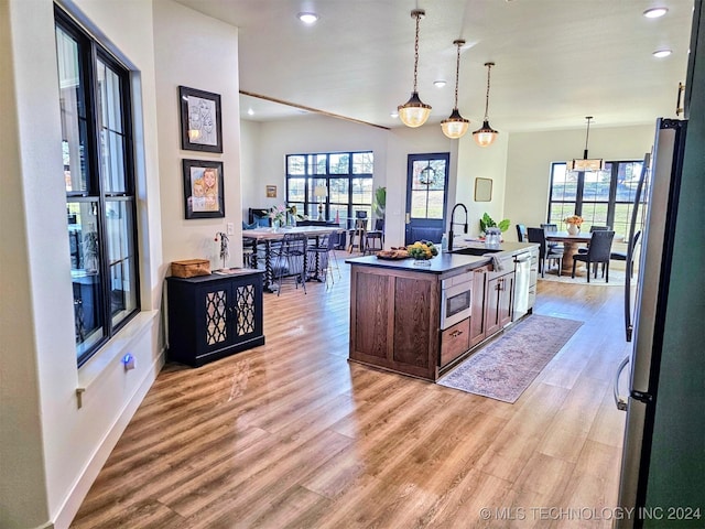 kitchen with sink, decorative light fixtures, a center island with sink, light wood-type flooring, and stainless steel appliances