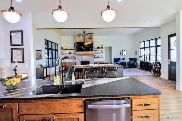 kitchen with sink, light wood-type flooring, dishwasher, pendant lighting, and a fireplace