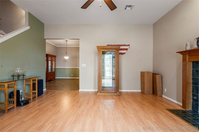 living room featuring a tiled fireplace, light hardwood / wood-style floors, ceiling fan, and crown molding