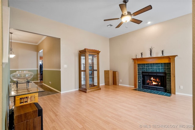 living room featuring ceiling fan, hardwood / wood-style flooring, a tiled fireplace, and ornamental molding