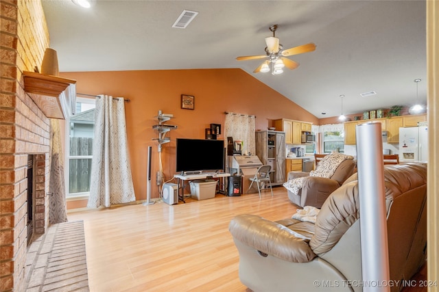 living room featuring light wood-type flooring, lofted ceiling, ceiling fan, and a brick fireplace