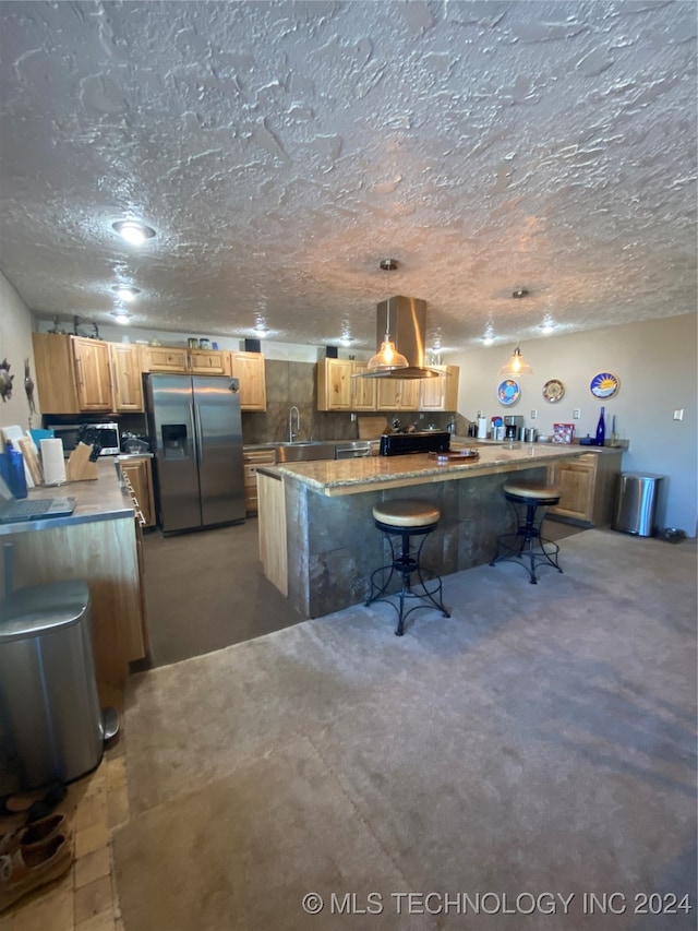 kitchen featuring island range hood, stainless steel refrigerator with ice dispenser, hanging light fixtures, a textured ceiling, and sink