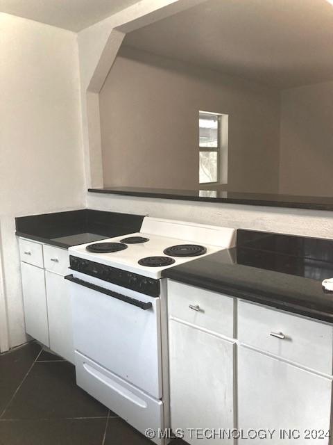 kitchen with electric range, white cabinetry, and dark tile patterned flooring