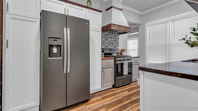 kitchen with white cabinets, custom exhaust hood, appliances with stainless steel finishes, and light hardwood / wood-style flooring