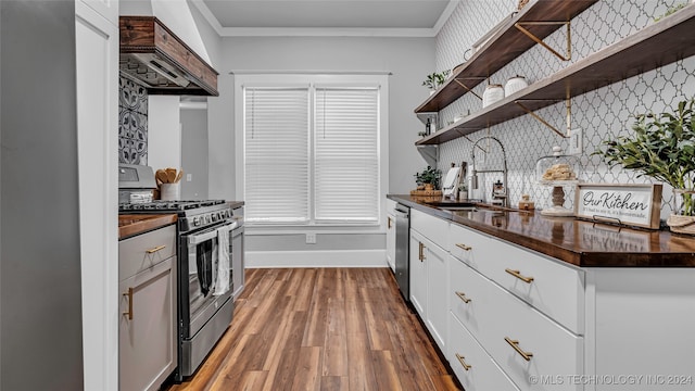 kitchen with stainless steel appliances, white cabinets, hardwood / wood-style floors, crown molding, and premium range hood