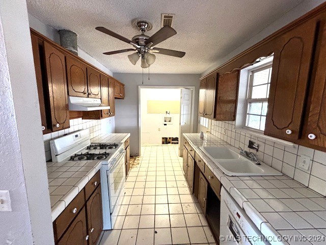 kitchen featuring white range with gas cooktop, tile countertops, sink, tasteful backsplash, and light tile patterned flooring