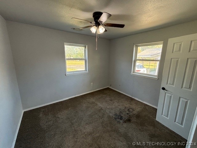 unfurnished room with a healthy amount of sunlight, a textured ceiling, and dark carpet