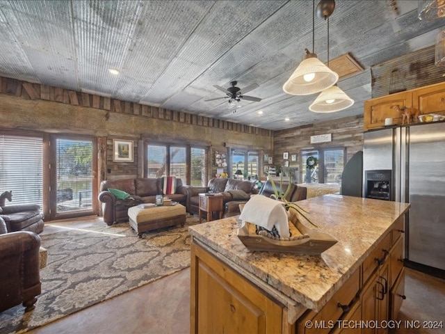 kitchen featuring pendant lighting, stainless steel refrigerator with ice dispenser, light stone countertops, ceiling fan, and a center island