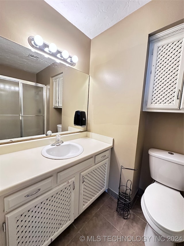 bathroom featuring tile patterned flooring, a textured ceiling, vanity, a shower with shower door, and toilet