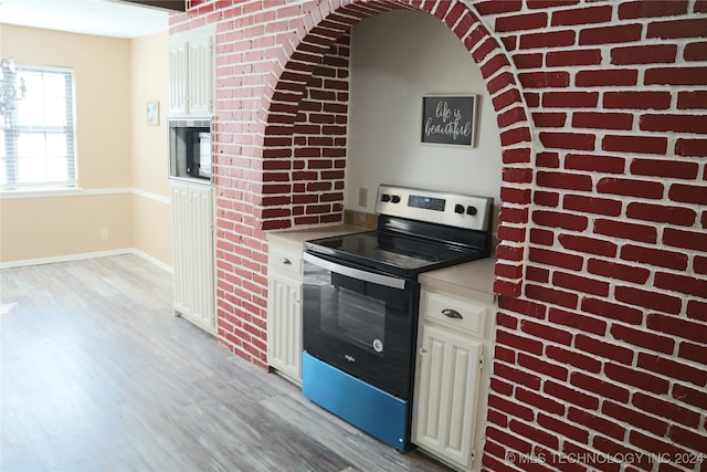 kitchen featuring white cabinets, light hardwood / wood-style floors, stainless steel range with electric stovetop, and brick wall