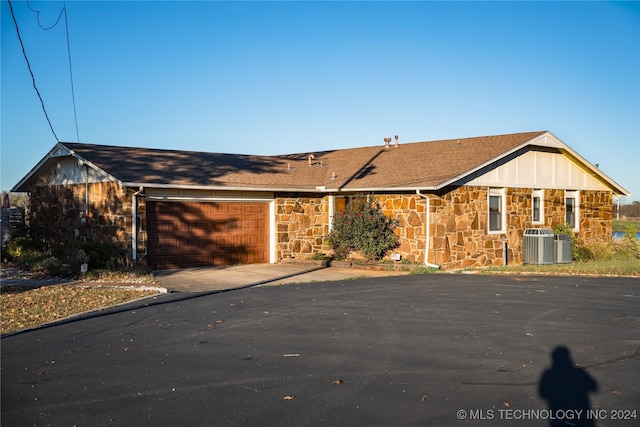 ranch-style house featuring an attached garage, stone siding, and driveway