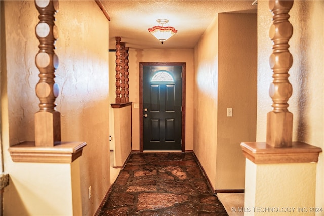 doorway to outside with a textured ceiling, a textured wall, and baseboards