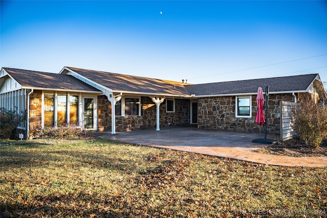 back of house with board and batten siding, stone siding, a lawn, and a patio