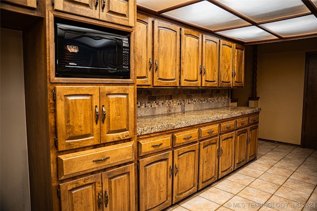 kitchen with black microwave, light tile patterned floors, and brown cabinets