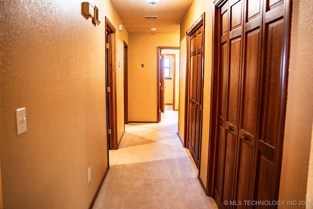 hallway with light colored carpet and a textured ceiling