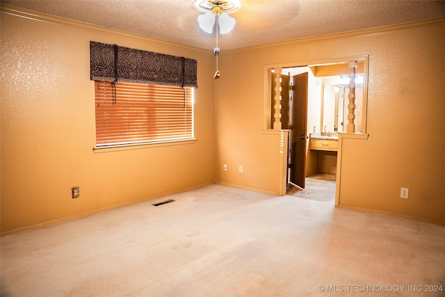 carpeted spare room with visible vents, baseboards, a ceiling fan, ornamental molding, and a textured ceiling