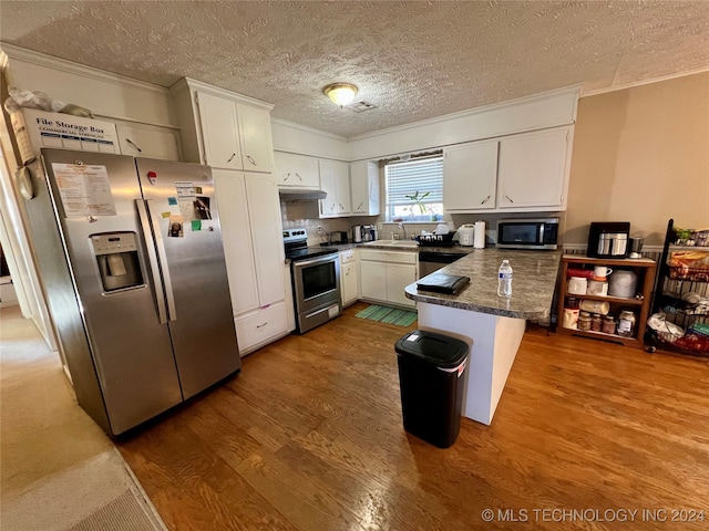 kitchen with stainless steel appliances, wood-type flooring, white cabinetry, and a textured ceiling