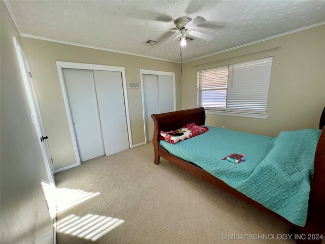 bedroom with crown molding, a textured ceiling, light carpet, two closets, and ceiling fan