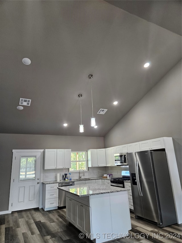 kitchen featuring dark wood-type flooring, appliances with stainless steel finishes, decorative light fixtures, a kitchen island, and white cabinetry