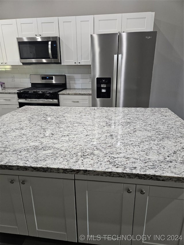 kitchen featuring light stone countertops, decorative backsplash, white cabinets, and stainless steel appliances