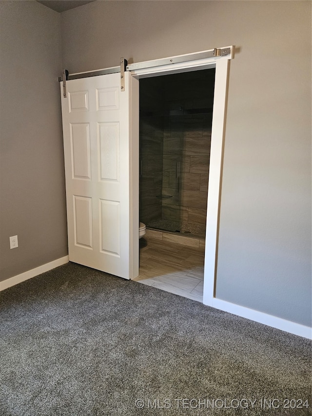 unfurnished bedroom featuring carpet flooring, a barn door, and ensuite bath