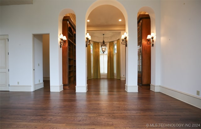 unfurnished room with decorative columns, dark wood-type flooring, and a notable chandelier