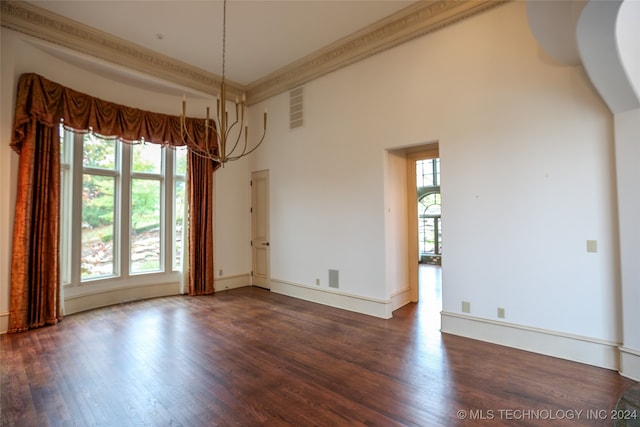 unfurnished room with a towering ceiling, an inviting chandelier, dark wood-type flooring, and crown molding