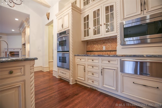 kitchen with appliances with stainless steel finishes, tasteful backsplash, crown molding, dark wood-type flooring, and dark stone countertops