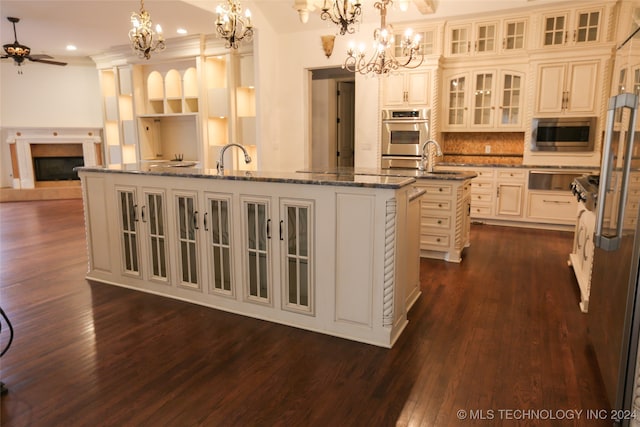 kitchen with stainless steel appliances, an island with sink, dark hardwood / wood-style floors, and decorative light fixtures