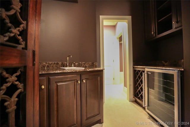 bar with dark brown cabinetry, sink, beverage cooler, dark stone countertops, and light carpet