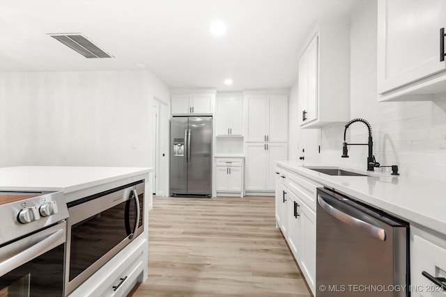 kitchen with light hardwood / wood-style floors, white cabinetry, sink, and appliances with stainless steel finishes