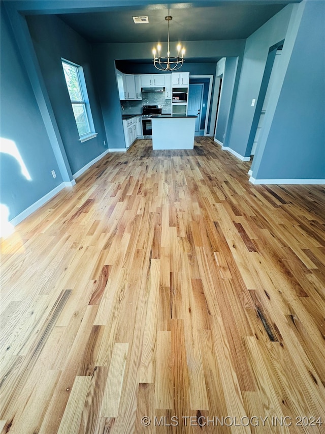 interior space with stainless steel stove, a notable chandelier, decorative light fixtures, white cabinets, and light wood-type flooring