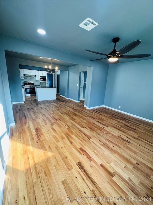 unfurnished living room featuring ceiling fan with notable chandelier and light hardwood / wood-style floors