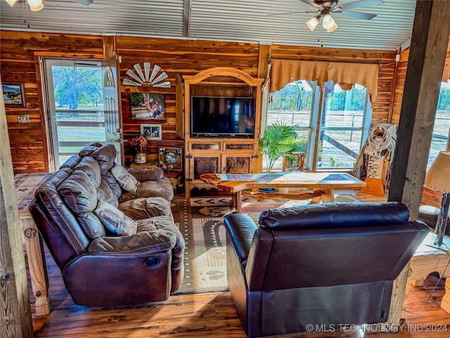 living room featuring hardwood / wood-style floors, wood walls, a healthy amount of sunlight, and ceiling fan