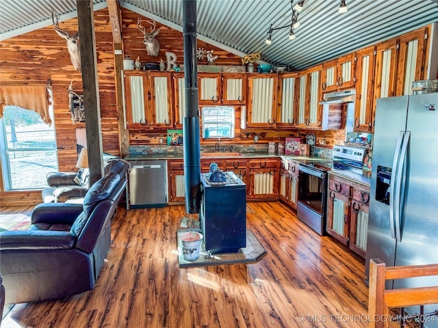 kitchen featuring lofted ceiling, wooden walls, appliances with stainless steel finishes, and hardwood / wood-style flooring