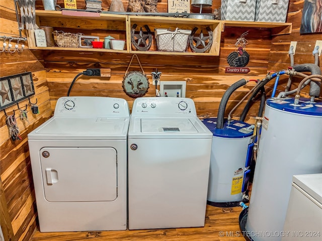 laundry area featuring water heater, wood walls, hardwood / wood-style flooring, electric water heater, and washer and clothes dryer