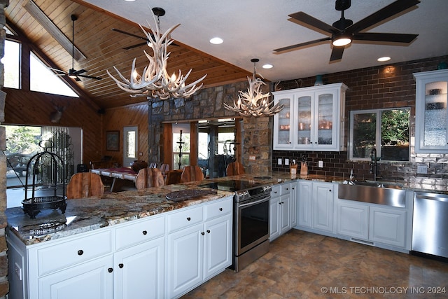 kitchen featuring pendant lighting, wooden walls, sink, white cabinetry, and appliances with stainless steel finishes