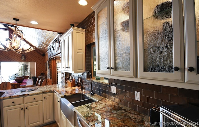 kitchen featuring an inviting chandelier, wood walls, sink, stone counters, and decorative light fixtures