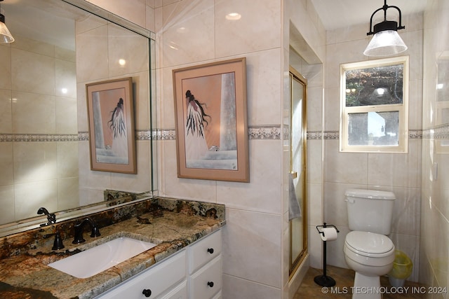 bathroom featuring a shower with shower door, vanity, toilet, and tile walls