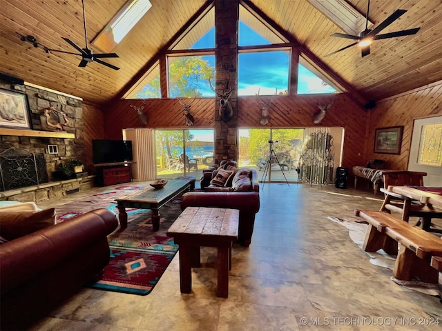 living room featuring ceiling fan, a skylight, high vaulted ceiling, wood ceiling, and wooden walls