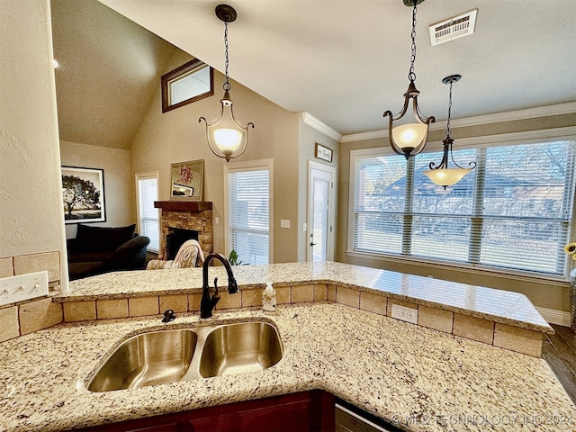 kitchen featuring vaulted ceiling, a stone fireplace, decorative light fixtures, sink, and ornamental molding