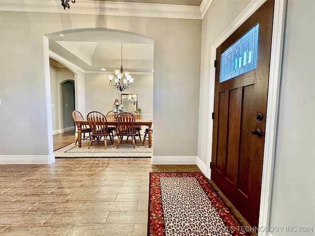 foyer featuring crown molding, wood-type flooring, a tray ceiling, and a chandelier