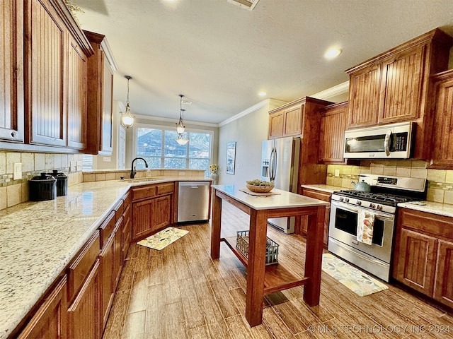 kitchen featuring sink, crown molding, hanging light fixtures, stainless steel appliances, and light hardwood / wood-style floors