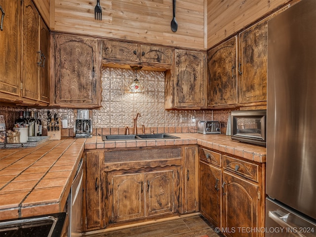 kitchen featuring stainless steel appliances, tile counters, a sink, and decorative backsplash