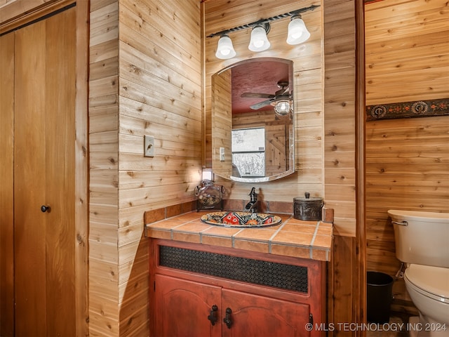 bathroom featuring a ceiling fan, wood walls, vanity, and toilet