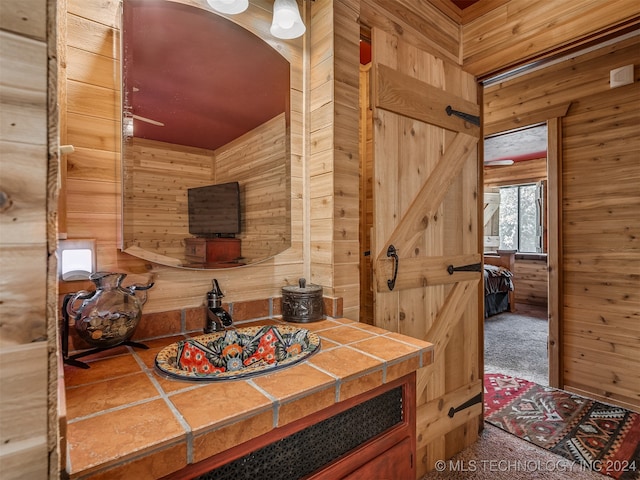 interior space with carpet floors, wood walls, tile countertops, and a barn door