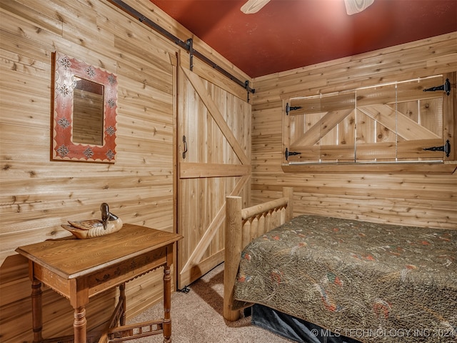 bedroom with carpet flooring, wooden walls, a barn door, and ceiling fan